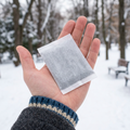 Broad rectangular hand warmer resting in one open palm outdoors