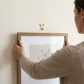 Person positioning a picture frame beneath a small wall hook